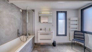 A modern bathroom with a bathtub, a sink, a mirror, and a window. - La Dépendance, Magnifique maison climatisée avec jardin (Bordeaux)