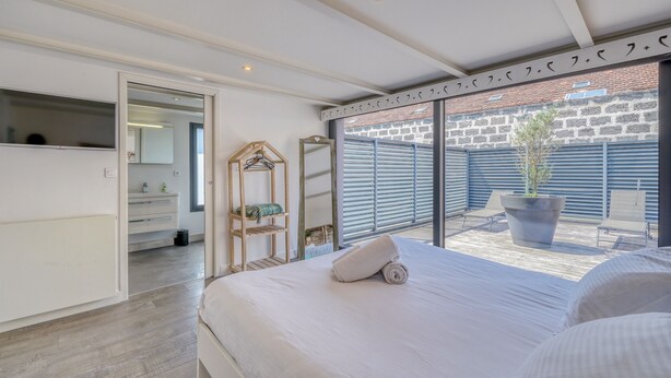 A bedroom with a large bed, a walk-in closet, and a view of a courtyard with a potted plant. - La Dépendance, Magnifique maison climatisée avec jardin (Bordeaux)