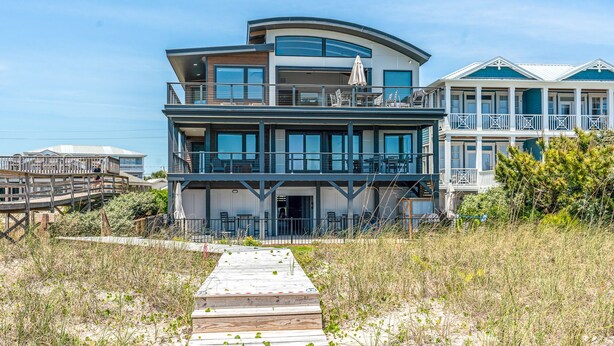 Propiedad frente al mar de varios pisos con una terraza de madera que conduce a la entrada, con balcones y ventanas amplias.