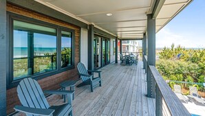 Un balcón techado con vistas al océano, terraza de madera y mobiliario exterior.