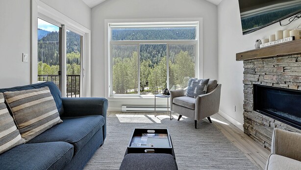 Ein modernes Wohnzimmer mit Kamin aus Naturstein, einem großen Fenster mit Bergblick und einer gemütlichen Sitzecke.