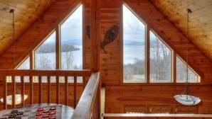 A cabin with a high ceiling and large windows offering views of a lake and mountains. - 60 West - Beautiful home with STUNNING view of Rangeley Lake (Rangeley)