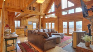 A spacious cabin interior with a large wooden dining table, a leather sofa, and a cozy fireplace. - 60 West - Beautiful home with STUNNING view of Rangeley Lake (Rangeley)