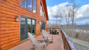 A wooden cabin with a deck, two Adirondack chairs, a table, and a scenic view of trees and mountains. - 60 West - Beautiful home with STUNNING view of Rangeley Lake (Rangeley)
