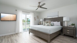 A bedroom with a large bed, a ceiling fan, a TV, a nightstand, and a sliding glass door to a balcony. - Large 5BR Home | Pool, Bonus Rooms & Walk to Beach & Dining (Fort Myers Beach)