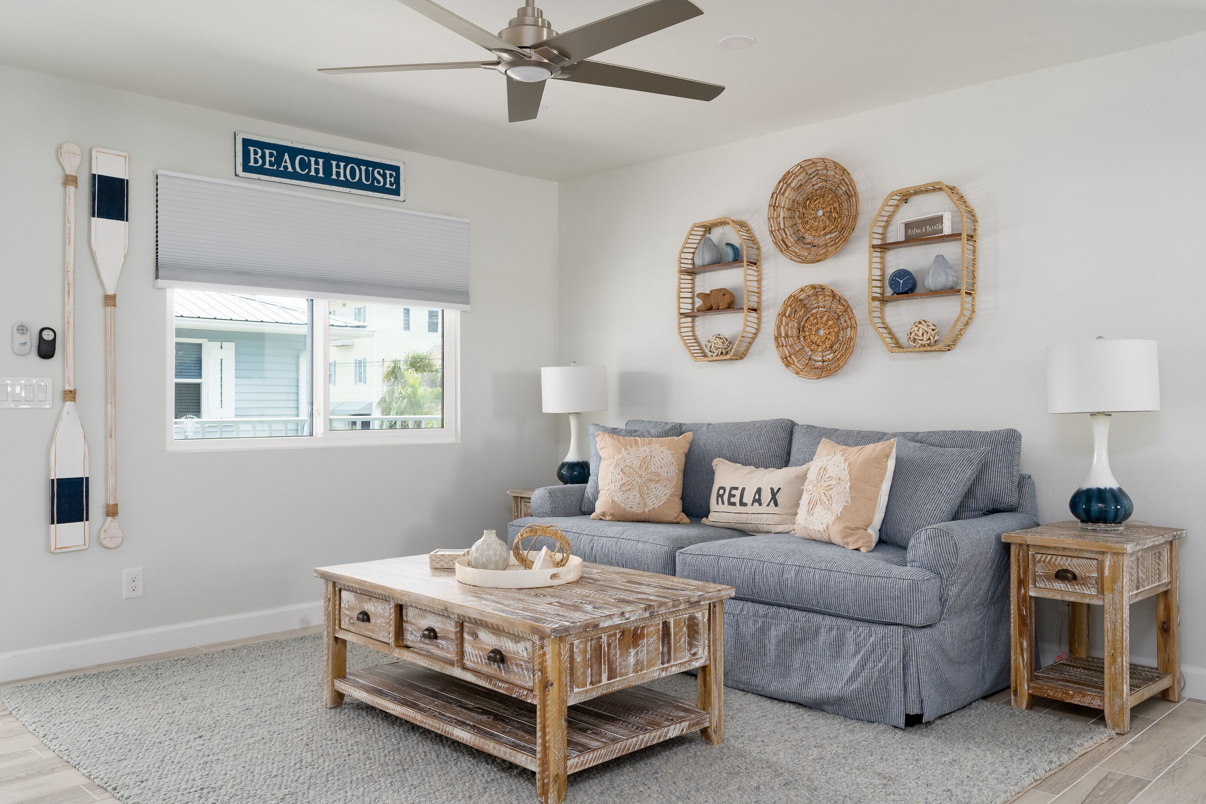Een woonkamer met een blauwe bank, een houten salontafel en een bordje met de tekst 'BEACH HOUSE'.
