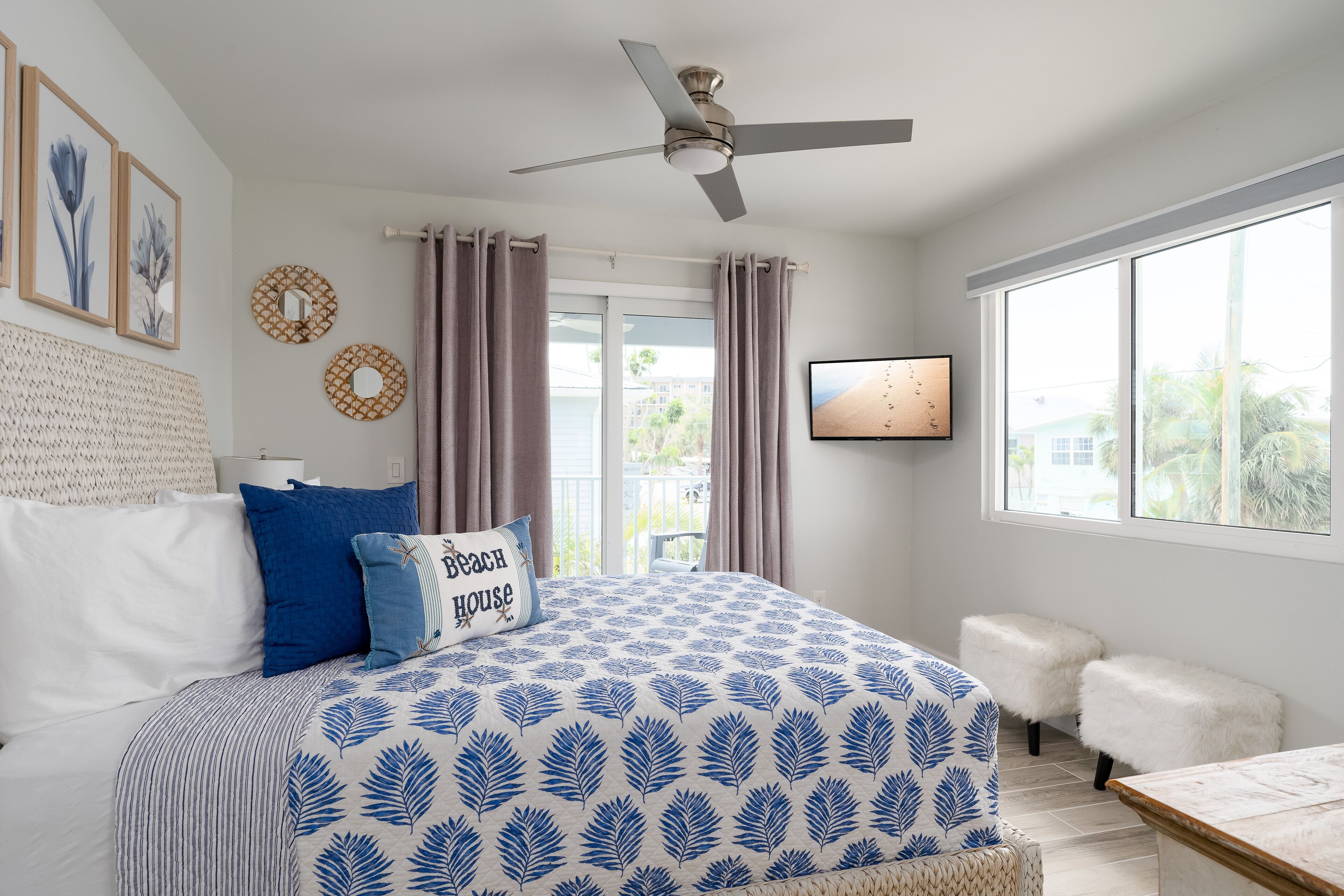 A bedroom with a bed, a ceiling fan, a TV, and a window with curtains.