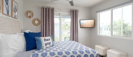 A bedroom with a bed, a ceiling fan, a TV, and a window with curtains.