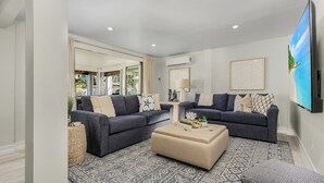 A modern living room with two dark sofas, a beige ottoman, and a patterned rug. - Large 5BR Home | Pool, Bonus Rooms & Walk to Beach & Dining (Fort Myers Beach)