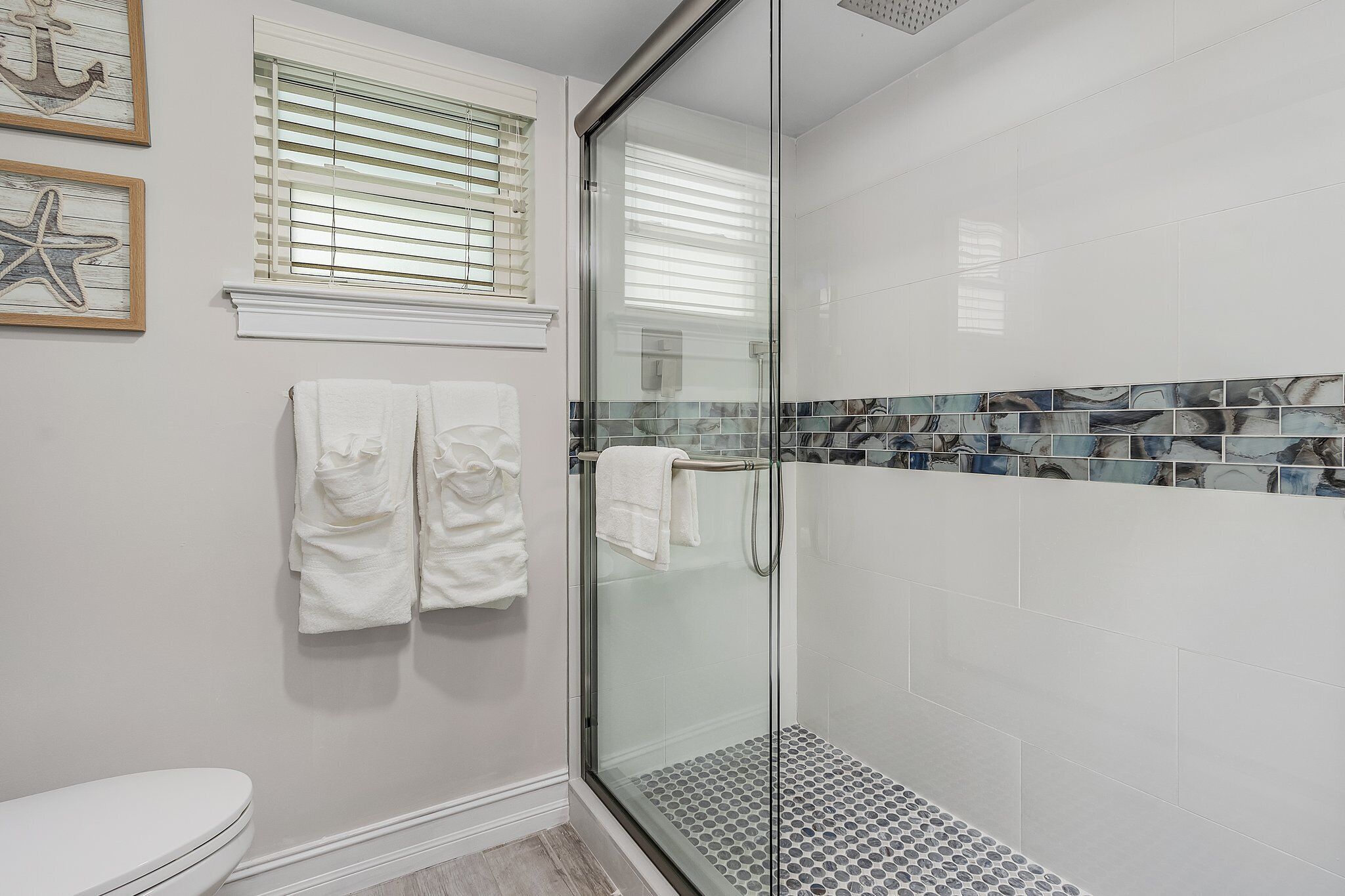 Un baño moderno con ducha envuelta en vidrio, azulejos blancos y decoración náutica en las paredes.