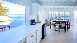Una cocina moderna con una isla grande, un comedor con mesa y sillas, y vistas al océano.