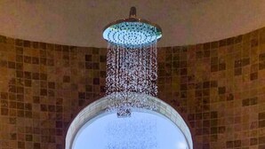 Un baño con cabezal de ducha sobre un ventanal, con vista a una isla distante.