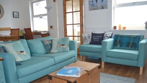 Ein Wohnzimmer mit einem sesselartigen Sofa in Türkis, einer Holzkommode und Blick durch ein großes Fenster.