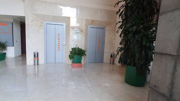 A spacious lobby with marble flooring, two elevators, and potted plants.