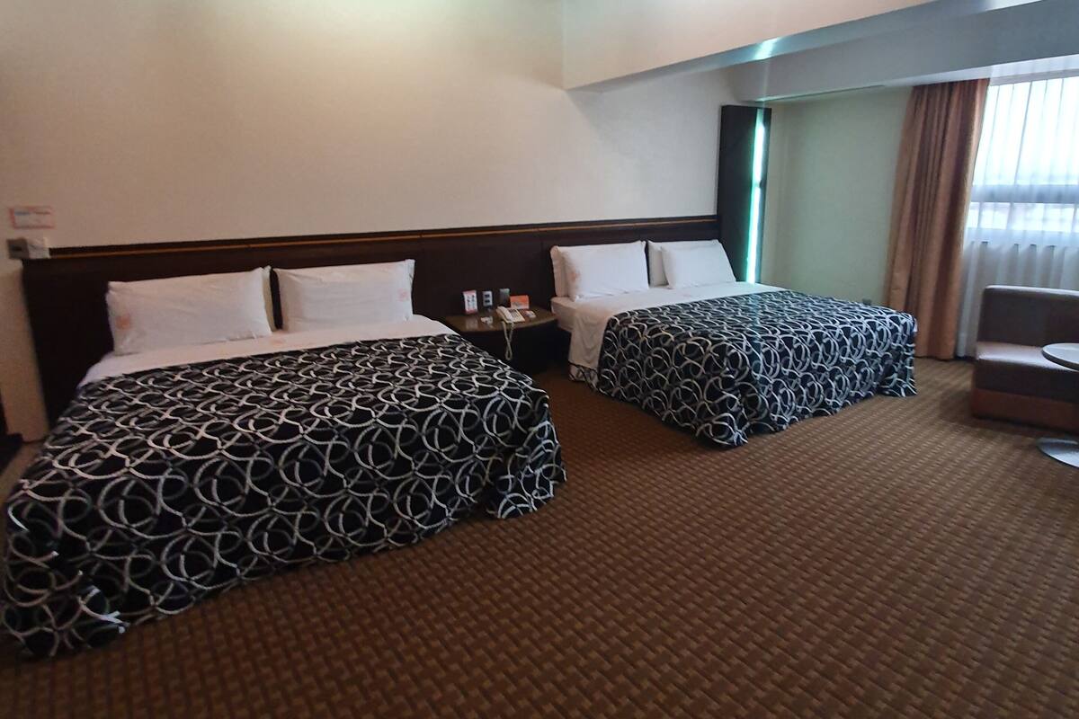 Habitación de hotel con dos camas, una mesita y una ventana con cortinas.