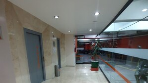 A modern hallway with a marble floor, a door labeled "ELEVATOR", and a glass railing overlooking a parking area. - Hotel Valle del Sur (Mexico City)