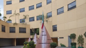 A building with a curved facade, multiple windows, and a central courtyard with decorative structures and a flag. - Hotel Valle del Sur (Mexico City)