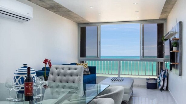 A modern living room with a glass table, a sofa, and a view of the ocean.