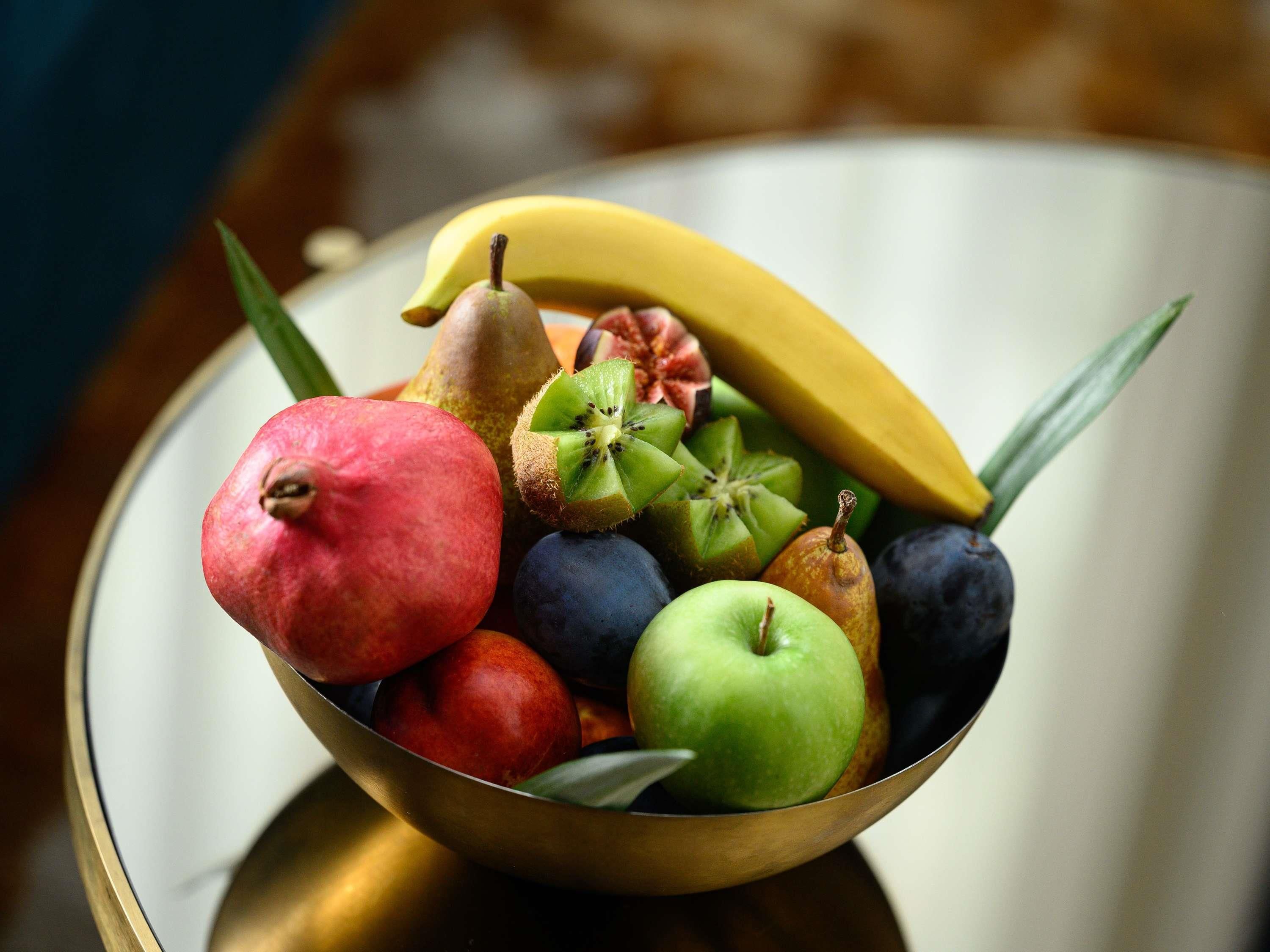 A bowl of assorted fruits including a pear, kiwi, apple, banana, and plum.
