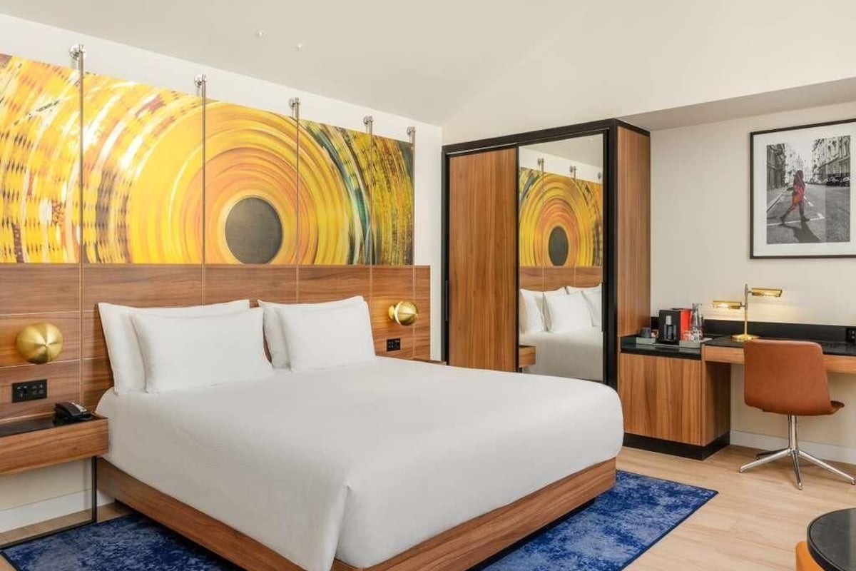 Quarto de hotel com uma cama grande, uma escrivaninha, uma cadeira e um espelho.