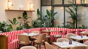 A restaurant with striped red and white seating, round tables, and hanging spherical lights. - Pullman Budapest (Budapest)