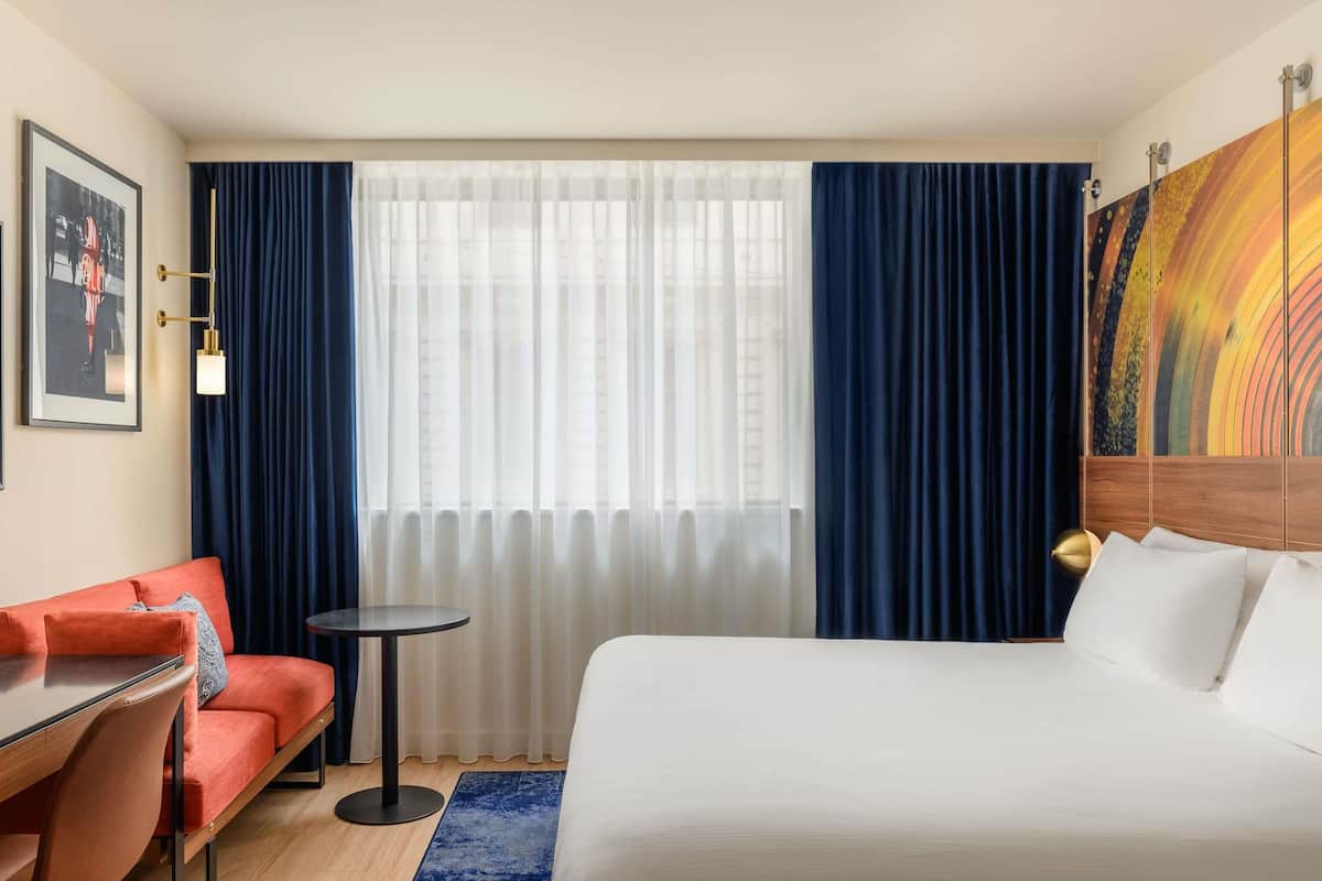 A hotel room with a bed, a sofa, a small table, and a painting on the wall.