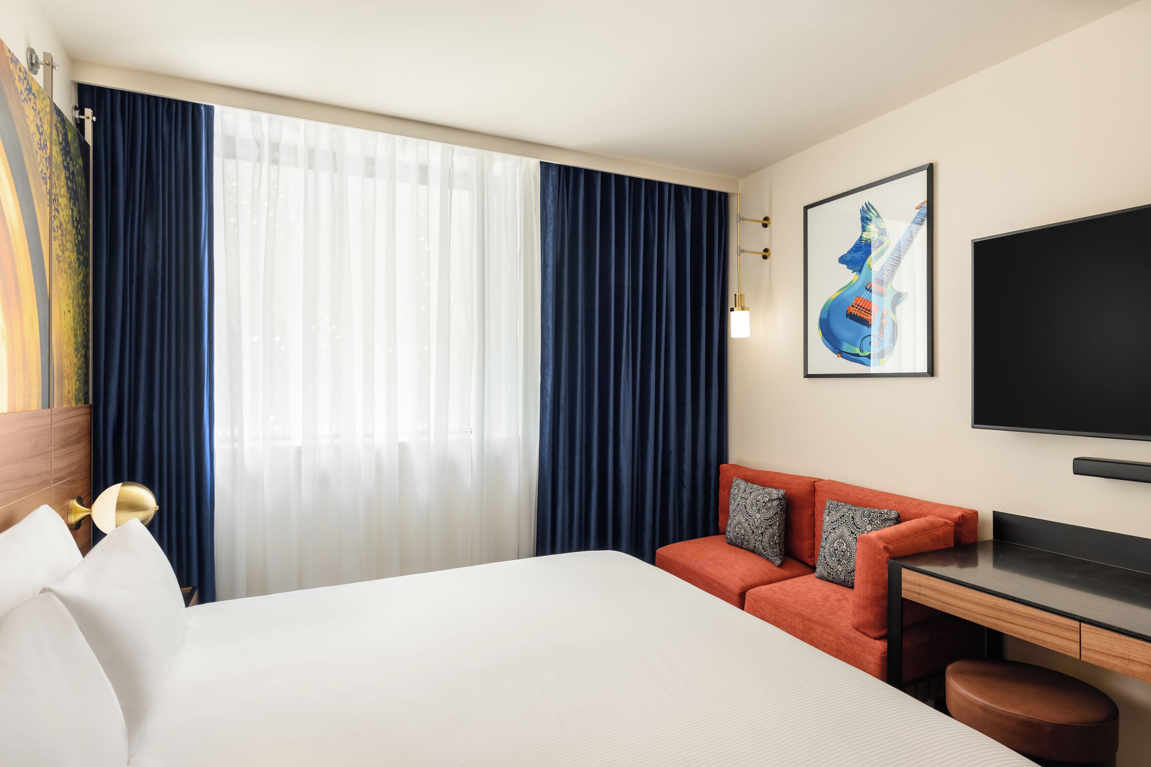 A hotel room with a bed, a desk, a chair, a TV, and a large window with curtains.