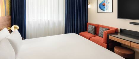 A hotel room with a bed, a desk, a chair, a TV, and a large window with curtains.
