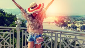 A person standing on a balcony with arms raised, overlooking a cityscape with a river and a bridge. - Pullman Budapest (Budapest)