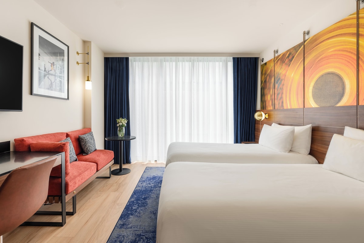 Quarto de hotel com cama, sofá, escrivaninha e um quadro na parede.
