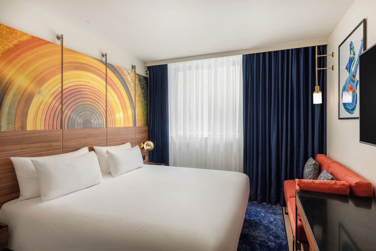 Quarto de hotel com cama grande, cabeceira de madeira, pintura, escrivaninha e cadeira.