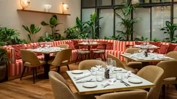 A restaurant with a cozy seating area, tables set with plates and glasses, and a large window with plants outside.