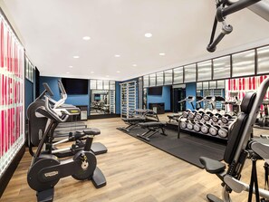 A gym with cardio machines, weightlifting equipment, and a mirror wall.