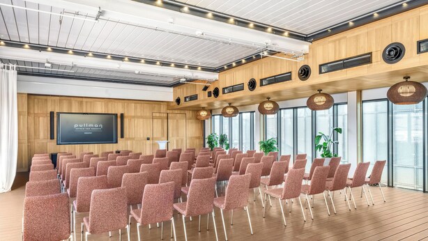 A conference room with rows of chairs, a large screen, and wooden paneling. - Pullman Budapest (Budapest)