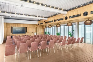 Un salón de conferencias con filas de sillas, una pantalla grande y paneles de madera.
