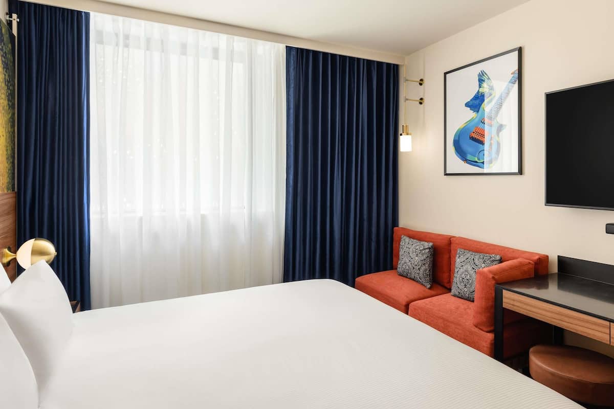 A hotel room with a bed, a desk, a chair, a TV, and a painting on the wall.