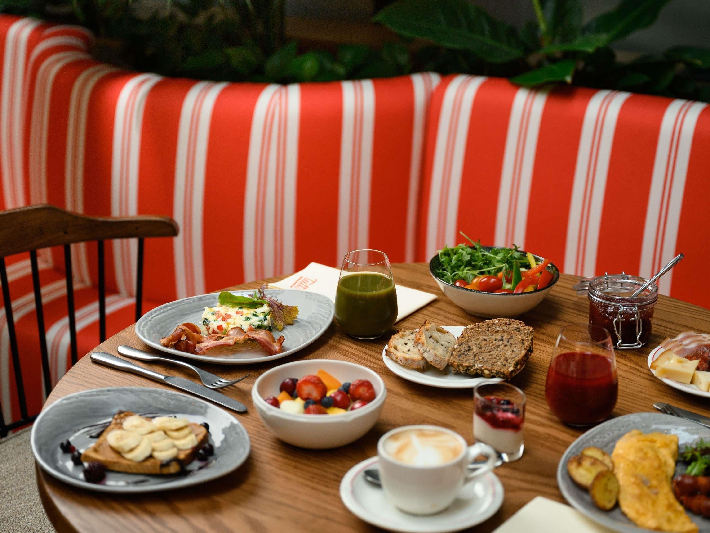 Uma mesa de jantar com diversos itens de café da manhã, um copo de suco verde e uma tigela de salada.