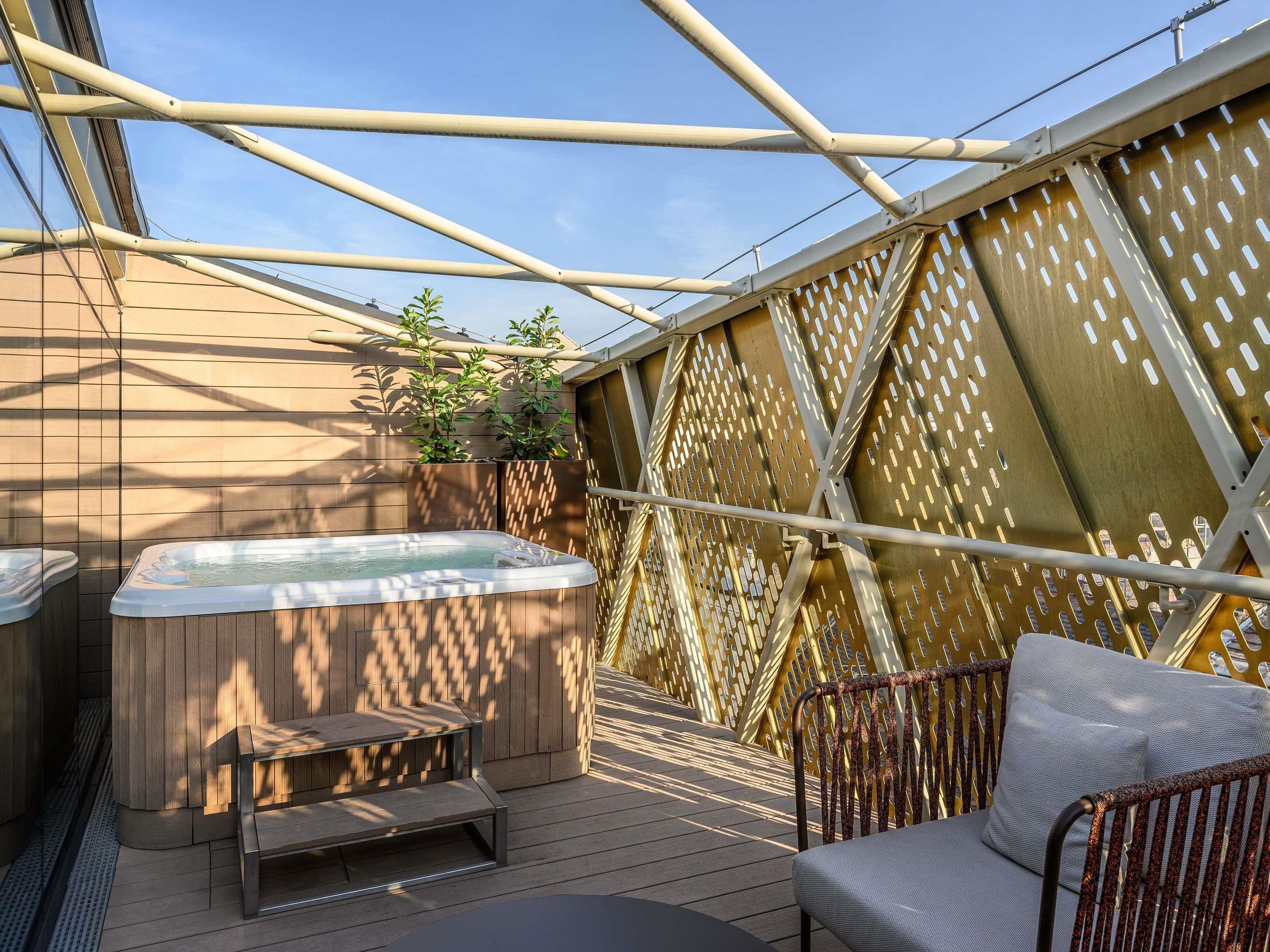 Een jacuzzi, houten terras, metalen stoel en een pergola.