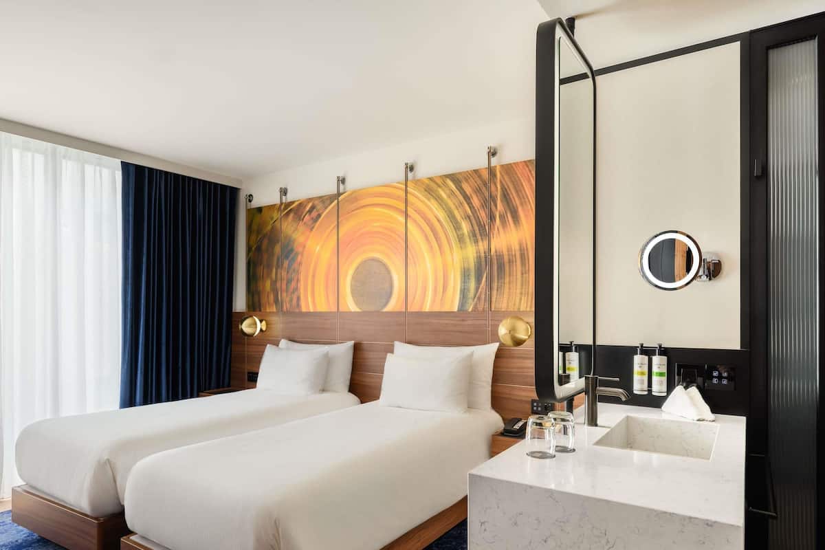 A hotel room with a large bed, a bathroom with a mirror, and a view of the city.