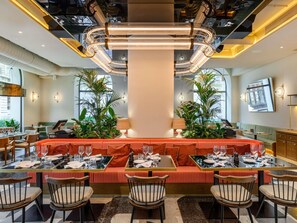 A restaurant with a central bar area, seating arrangements, and a modern ceiling design. - Pullman Budapest (Budapest)