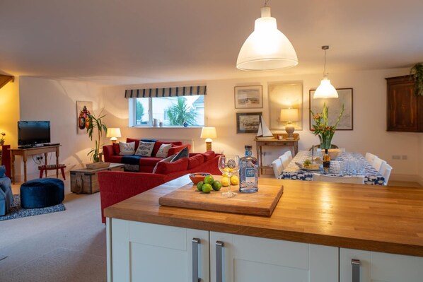 A modern kitchen with a wooden countertop, red sofa, dining table with blue tablecloth, and a large window with curtains.