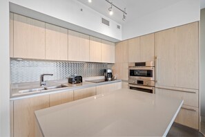 A modern kitchen with light wood cabinets, a large island, stainless steel appliances, and a tiled backsplash.