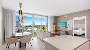 A modern hotel room with a balcony, a dining area, a sofa, a TV, and a bed.