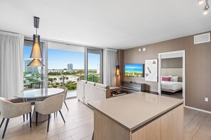 A modern hotel room with a balcony, a dining area, a TV, and a bed.