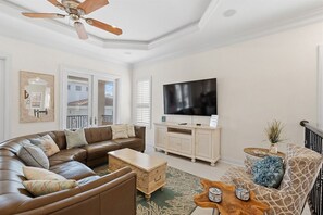 Een woonkamer met een grote flatscreen televisie, een bruine leren bank, een houten salontafel en een kamerkleed met een patroon.