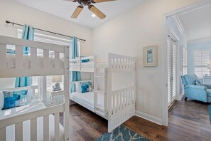 A bedroom with bunk beds, a ceiling fan, a window with blinds, and a blue armchair.