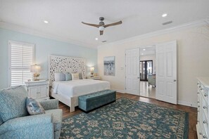 A bedroom with a bed, a bench, a chair, a ceiling fan, and a door.