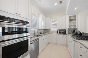 A modern kitchen with white cabinetry, stainless steel appliances, and a marble countertop.