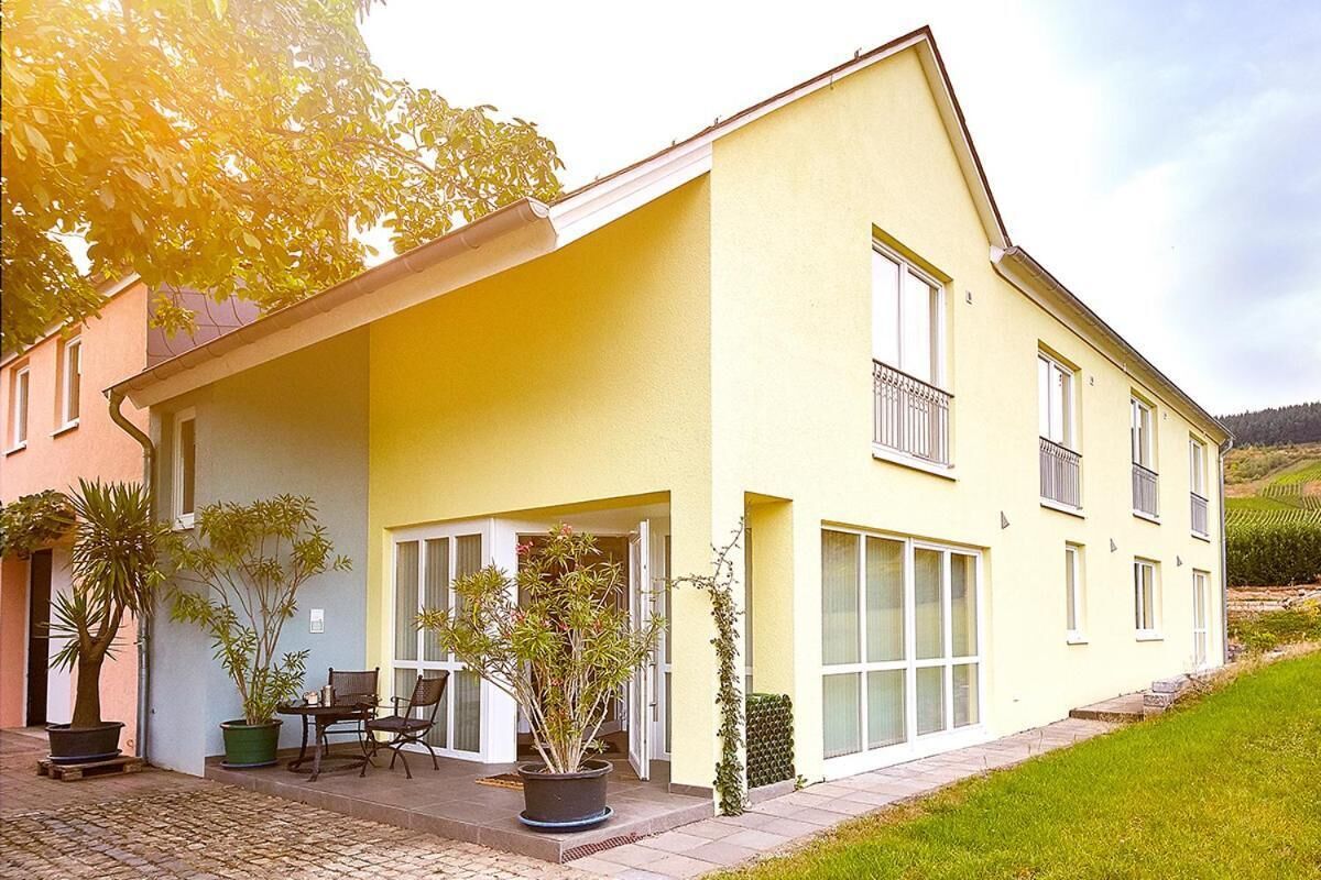 Ein gelbes, zweistöckiges Haus mit einer Veranda, Blumentöpfen und einer kleinen Sitzgruppe im Freien.
