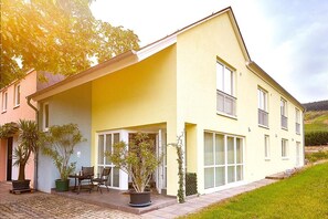 A yellow two-story house with a covered porch, potted plants, and a small outdoor seating area. - GästeHaus Auler Hof (Kröv)